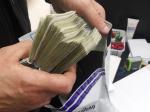 Funkcjonariusz wkłada gruby plik banknotów do bezpiecznej koperty