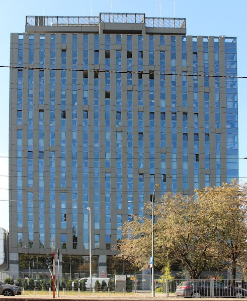 Budynek Mazowieckiego Urzędu Celno-Skarbowego w Warszawie. Przed budynkiem ulica i jadące samochody.