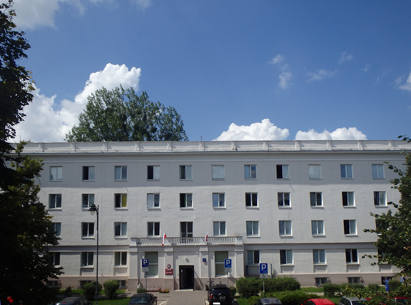 Budynek Urzędu Skarbowego Warszawa-Bielany. Przed budynkiem parking, a na nim kilka samochodów.