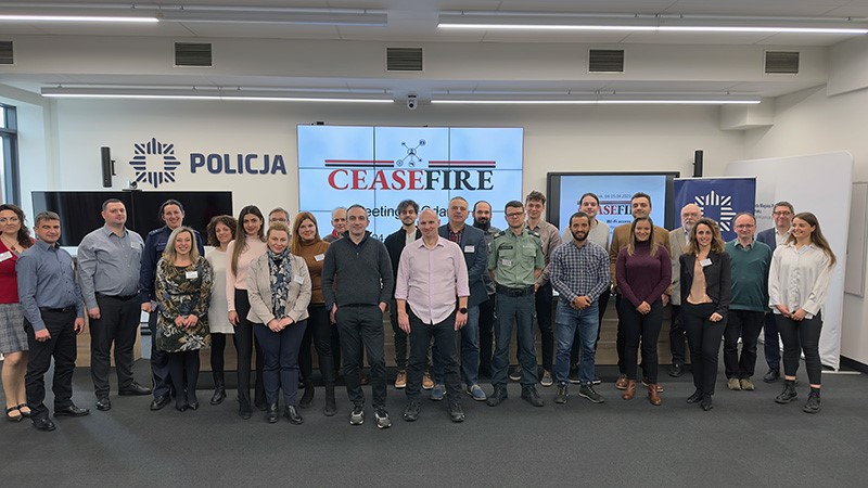 Grupa ludzi w dużej sali konferencyjnej. W tle tablica z logo projektu Ceasefire.