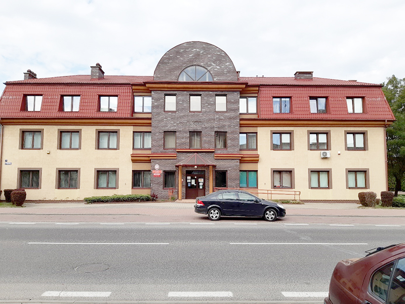 Budynek Urzędu Skarbowego w Przasnyszu, przed budynkiem ulica i samochód.