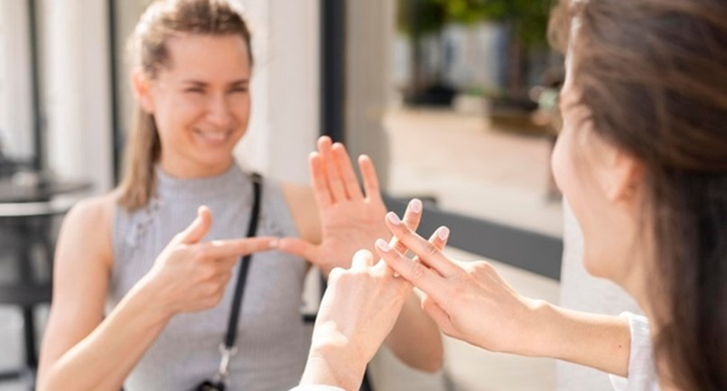 Dwie uśmiechnięte kobiety rozmawiające w języku migowym.