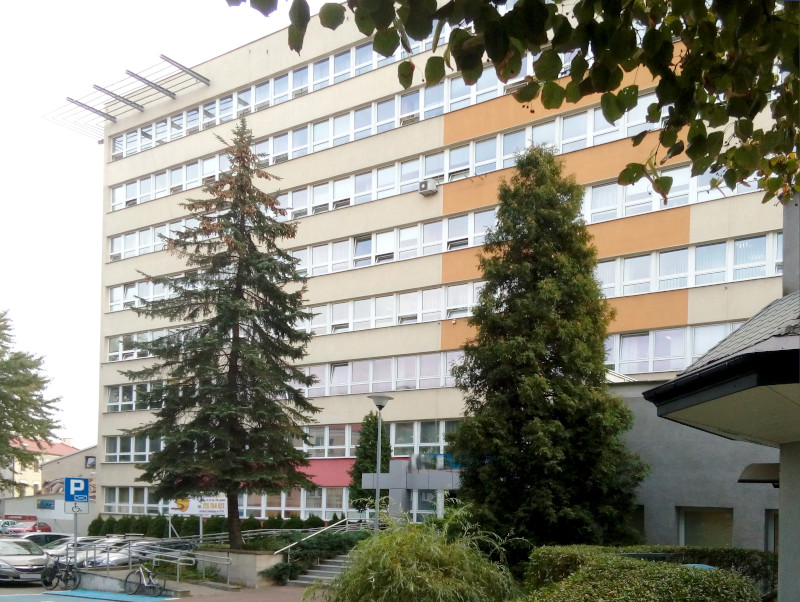 Budynek Trzeciego Mazowieckiego Urzędu Skarbowego w Radomiu. Przed budynkiem parking, samochody i drzewa.