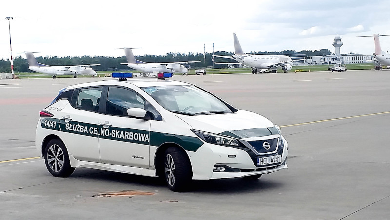 Samochód służbowy Służby Celno-Skarbowej na płycie lotniska, w tle samoloty stojące tyłem.
