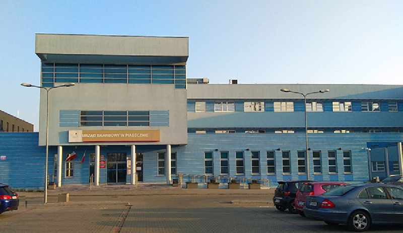 Budynek Urzędu Skarbowego w Piasecznie. Przed budynkiem parking i kilka samochodów.