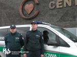 Dwóch funkcjonariuszy, za nimi samochód służbowy, ściana szpitala, na nij logo Centrum Zdrowia Dziecka