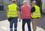 Dwóch funkcjonariuszy Służby Celno-Skarbowej prowadzi pod rękę podejrzanego o wyłudzenia podatku VAT 