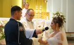 Ksiądz udziela młodej parze sakramentu małżeństwa, w tle celebrujący Mszę Świętą ksiądz kapelan Krajowej Administracji Skarbowej