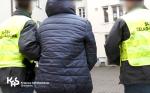 Jeden funkcjonariusz Służby Celno-Skarbowej prowadzi pod rękę podejrzanego. Obok idzie drugi funkcjonariusz