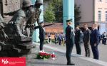 Dwie funkcjonariuszki pełniące wartę przy Pomniku Powstania Warszawskiego, trzy osoby oddające hołd poległym, wiązanka i znicze
