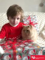 Krzyś z prezentem, obok siedzi kot, z tyłu torba prezentowa.