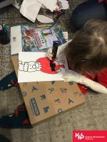 Krzyś siedzi na dywanie i maluje Mikołaja.