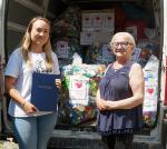 Dwie kobiety, jedna z nich trzyma podziękowanie, w tle samochód z nakrętkami.