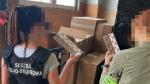Dwie funkcjonariuszki SCS kontrolują zawartość kartonów z paczkami przemyconych papierosów.
