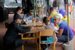 Dwoje celników i troje dzieci siedzących i rysujących przy stoliku w kąciku plastycznym