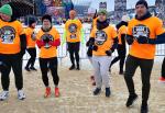 Kilka osób w pomarańczowych koszulkach rozgrzewa się przed biegiem.