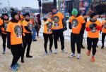 Grupa osób w pomarańczowych koszulkach rozgrzewa się przed biegiem.