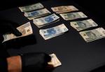 Ułożone w stosy polskie banknoty o nominale 50, 100 i 200 złotych na czarnej powierzchni, osoba licząca banknoty w czarnych rękawiczkach.