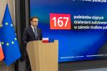 Mężczyzna w garniturze przemawia przy mównicy z flagami Polski i Unii Europejskiej w tle, obok wyświetlacz z liczbą 167 dotyczącą audytów środków publicznych.