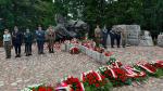 Pomnik z wieńcami i zapalonymi zniczami upamiętniający bohaterów, przed którym stoi warta honorowa w mundurach różnych służb.