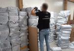 Funkcjonariusz Służby Celno-Skarbowej kontroluje dużą liczbę zapakowanych przesyłek w magazynie.