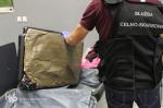 Funkcjonariusz Służby Celno-Skarbowej trzyma w ręku podwójne dno walizki z przyklejonymi do niego pakunkami