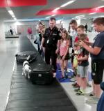 Dzieci oglądają psa Diunę, suczkę rasy jack russell terier, na taśmie wśród bagaży.